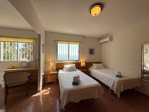 Une chambre d’hôtel avec deux lits simples, un bureau avec une chaise, une fenêtre donnant sur un paysage agréable et un appareil de climatisation.
