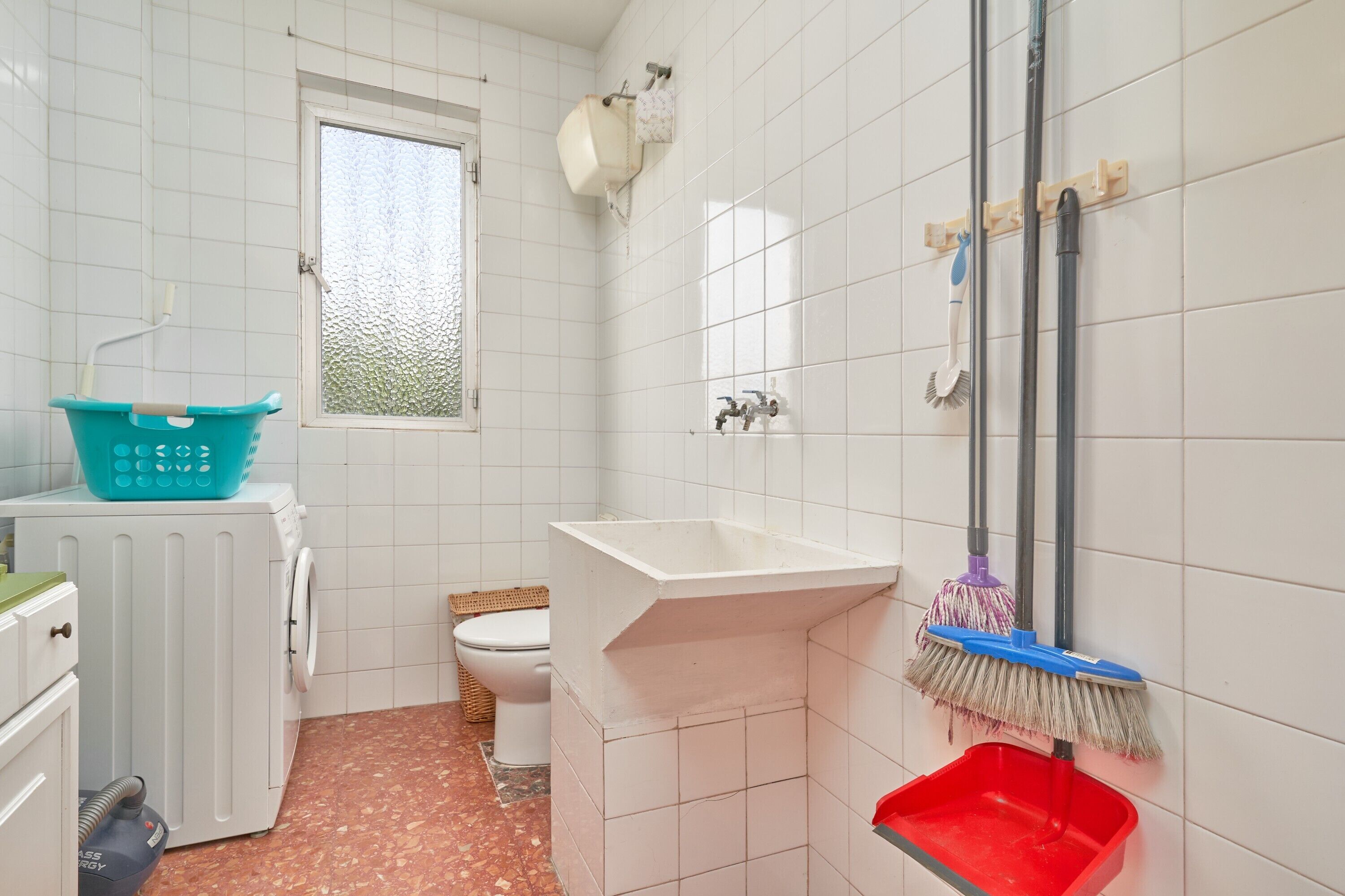 Ein kleines Badezimmer mit Waschmaschine, Toilette, Waschbecken und einem Mop.