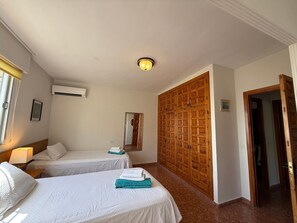 A hotel room with two beds, a wardrobe, a mirror, and an air conditioning unit.