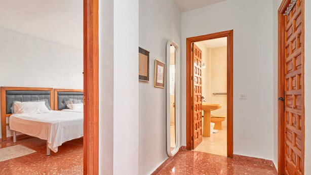 Habitación de hotel con una cama, un baño visible a través de una puerta abierta y un pasillo con una puerta de madera.