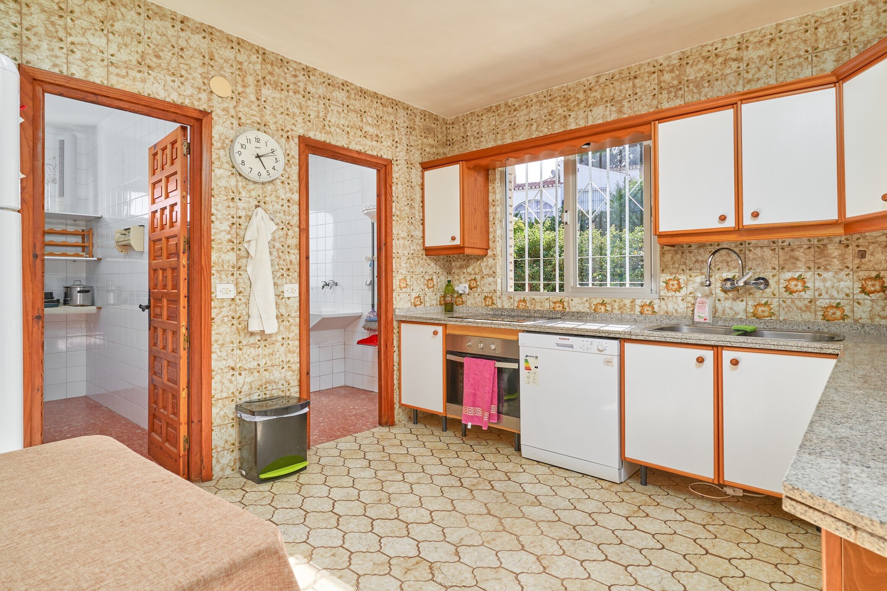 Cocina con alacenas blancas, un lavamanos, estufa y ventana con vista a follaje.