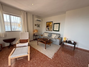 Un salon comprenant un canapé, un fauteuil, une table basse, une lampe et une petite table ornée d’objets décoratifs.