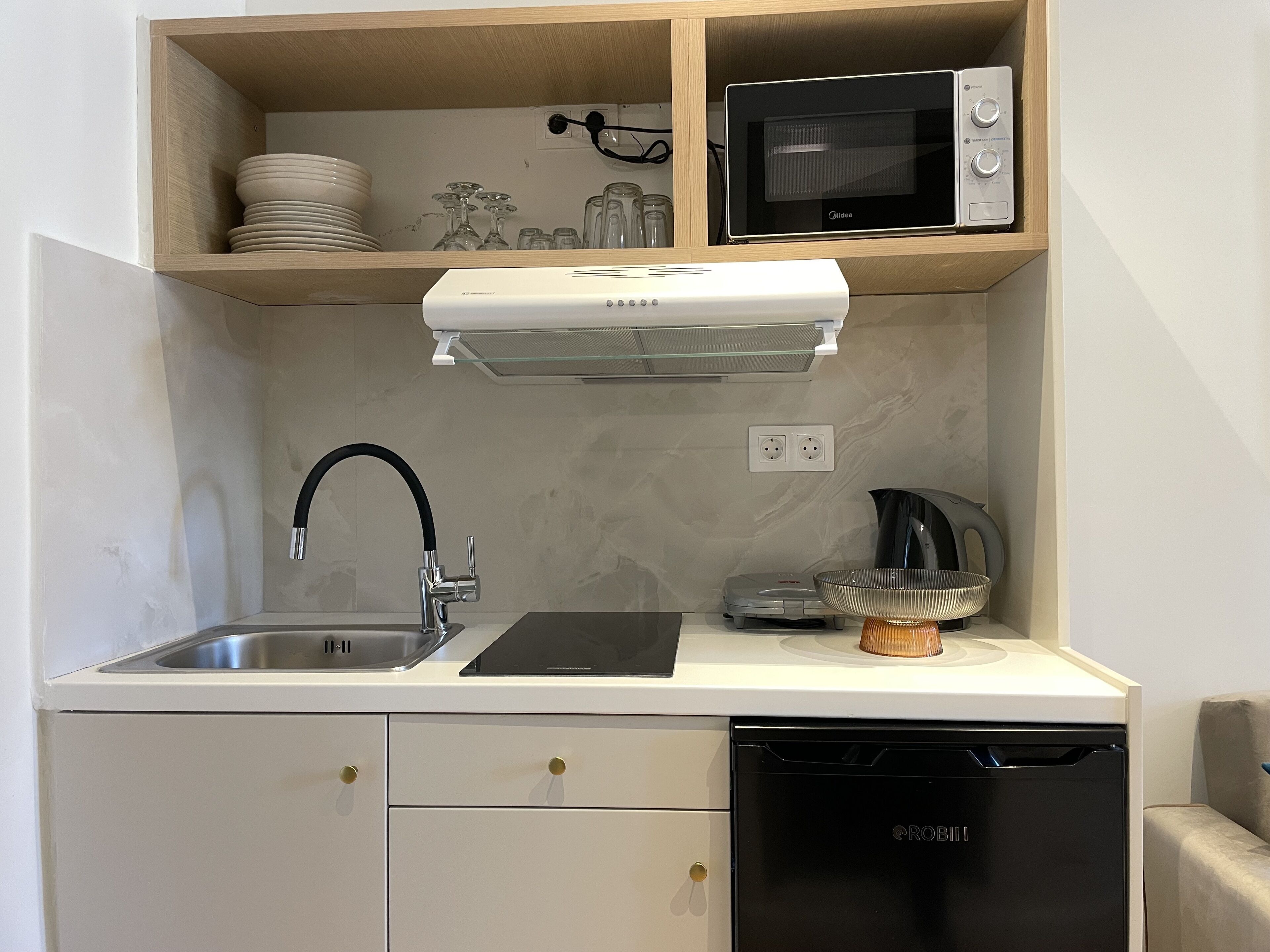 Eine kompakte Küche mit Mikrowelle, Toaster und Wasserkocher auf der Arbeitsfläche, einem Waschbecken mit modernem Wasserhahn und einem Geschirrspüler.