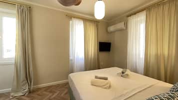 Habitación de hotel con cama, cortinas, aire acondicionado, televisión y suelo de madera.