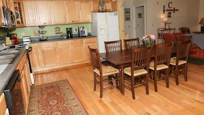 A kitchen with wooden cabinets, a dining table with chairs, a refrigerator, and a coffee maker.