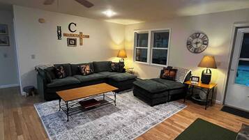 Ein Wohnzimmer mit Ecksofa, Couchtisch, Teppich, Lampe und einer Wanduhr.