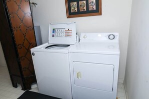 Una lavadora blanca con panel de control, una puerta con un diseño metálico decorativo y un cuadro en la pared.