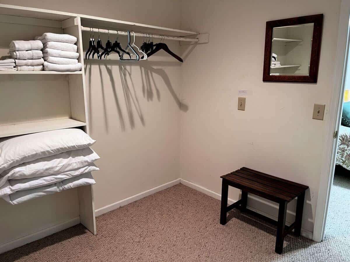 A closet with hanging clothes and shelves, a wooden bench, and a mirror on the wall.