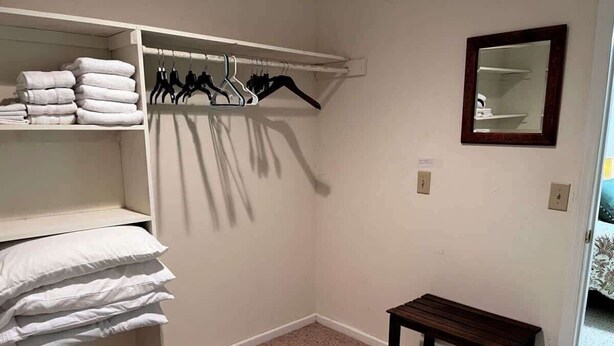 A closet with hanging clothes and shelves, a wooden bench, and a mirror on the wall.