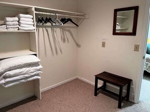Un armario con ropa colgada y estantes, un banco de madera y un espejo en la pared.