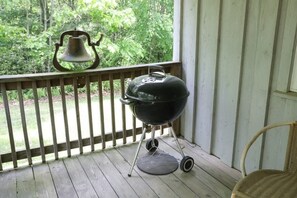 Una terraza de madera con una parrilla negra y una silla de mimbre.