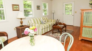 A living room with a green-striped sofa, a wooden coffee table, a dining table with a vase of flowers, and a wooden cabinet.