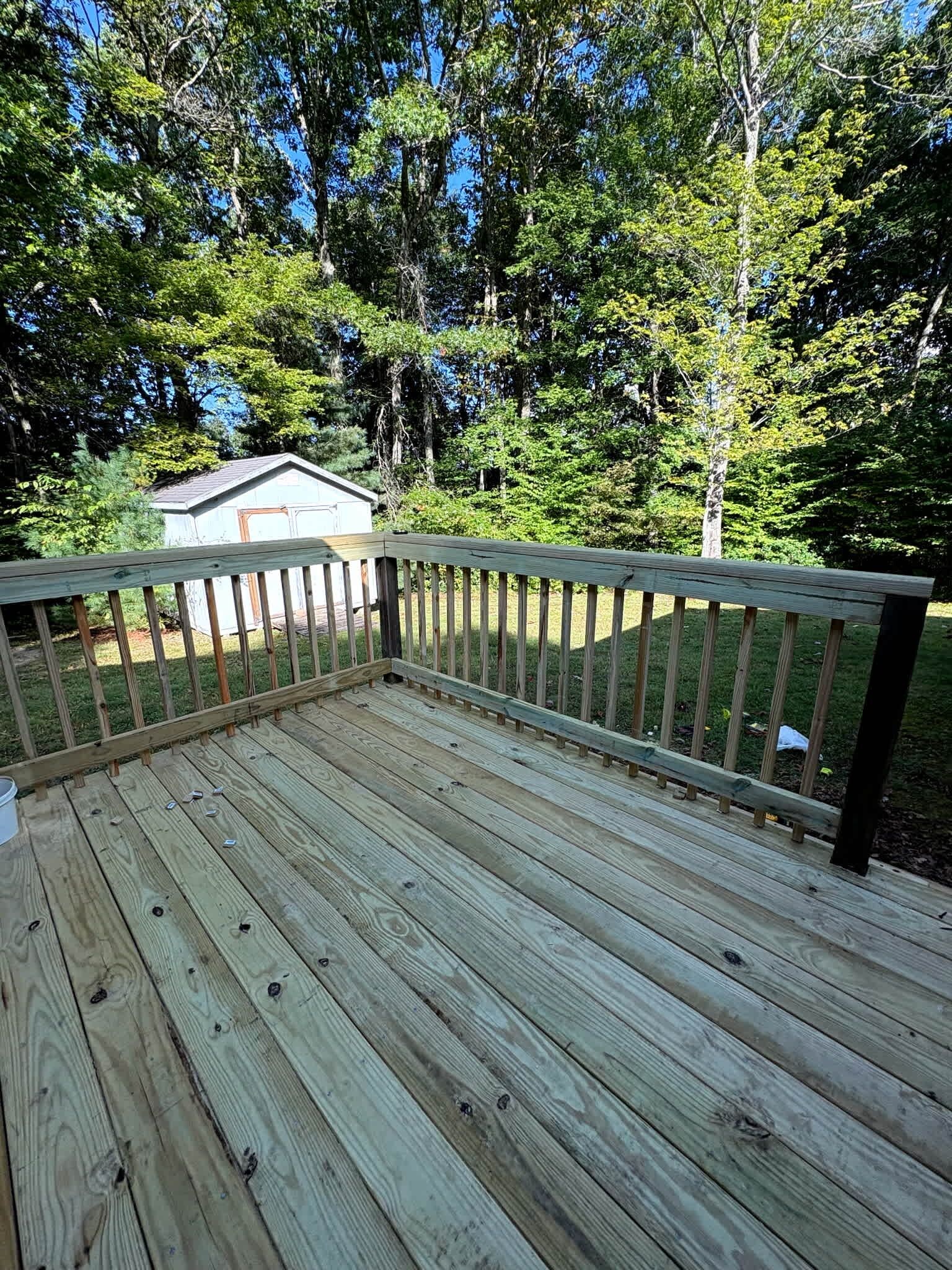 A wooden deck with railings, surrounded by trees and a house in the background.