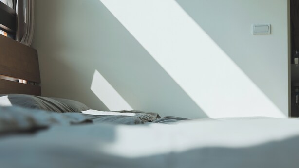 Een bed met hoofdbord, een lichtschakelaar en een raam dat schaduwen werpt.
