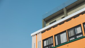 Een meerlaags gebouw met oranje en witte gevels, grote ramen met witte gordijnen, en een plat dak.