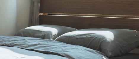 A bed with a wooden headboard, grey bedding, and a window with curtains.