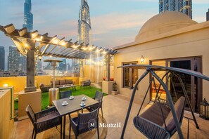 Une terrasse sur le toit avec des sièges extérieurs, une pergola illuminée de guirlandes lumineuses et un fauteuil suspendu.