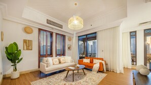 Ein geräumiges Wohnzimmer mit einem weißen Sofa, einem orangen Sofa, einem Couchtisch und einem großen Fenster mit Blick auf die Stadt.