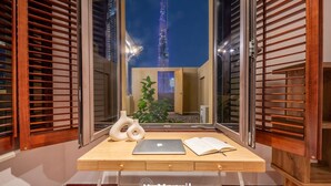Ein Schreibtisch mit einem Laptop, einem Buch, einer Pflanze und Blick auf den Burj Khalifa bei Nacht.