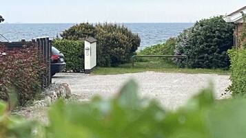 A coastal property with a driveway leading to a garage, a small white utility shed, and dense greenery.