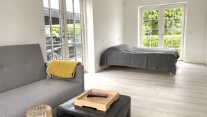 Ein modernes Wohnzimmer mit einem grauen Sofa, einem schwarzen Lederhocker, einer Glasvase und einem Holztablett mit einer Fernbedienung.