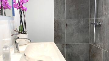 Ein modernes Badezimmer mit einem weißen Waschbecken, einer Duschbrause und einer Topfpflanze mit Orchideen.
