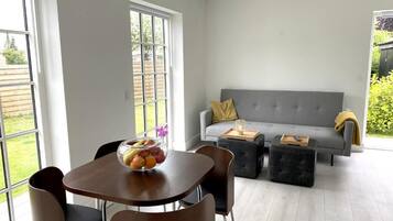 A modern living room with a grey sofa, two black ottomans, a wooden coffee table, and a dining table with chairs.