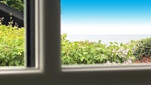 Blick durch ein Fenster auf einen Heckenstreifen und einen strahlend blauen Himmel.