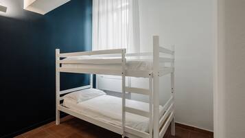Ein Stockbett in einem Raum mit blauen und weißen Wänden, einem Fenster mit weißen Vorhängen und einem gefliesten Boden.