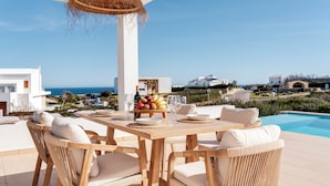 An outdoor dining area with wicker chairs and a table set for two, overlooking a pool and a coastal view. - Villa Mercedes - Warm and quiet villa without equal (Ciutadella de Menorca)
