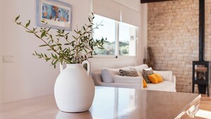 A white vase with green foliage on a wooden table in a room with a white sofa, a brick wall, and a framed picture on the wall. - Villa Mercedes - Warm and quiet villa without equal (Ciutadella de Menorca)