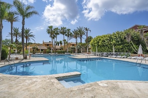 A swimming pool surrounded by palm trees and lounge chairs, with a building in the background.