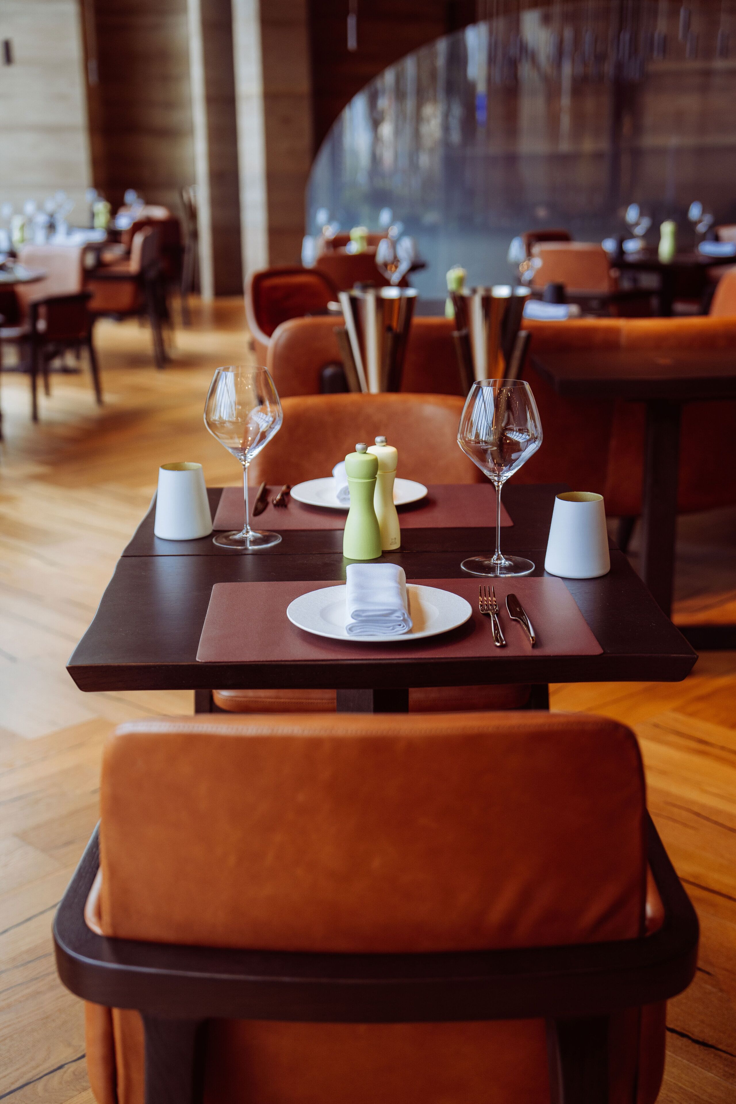 A restaurant setting with tables set for dining, featuring chairs, plates, cutlery, and wine glasses.