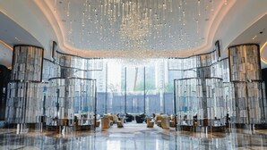 A spacious lobby with a high ceiling, modern chandeliers, and a view of the cityscape through large windows. - MGM Qingdao (Qingdao)