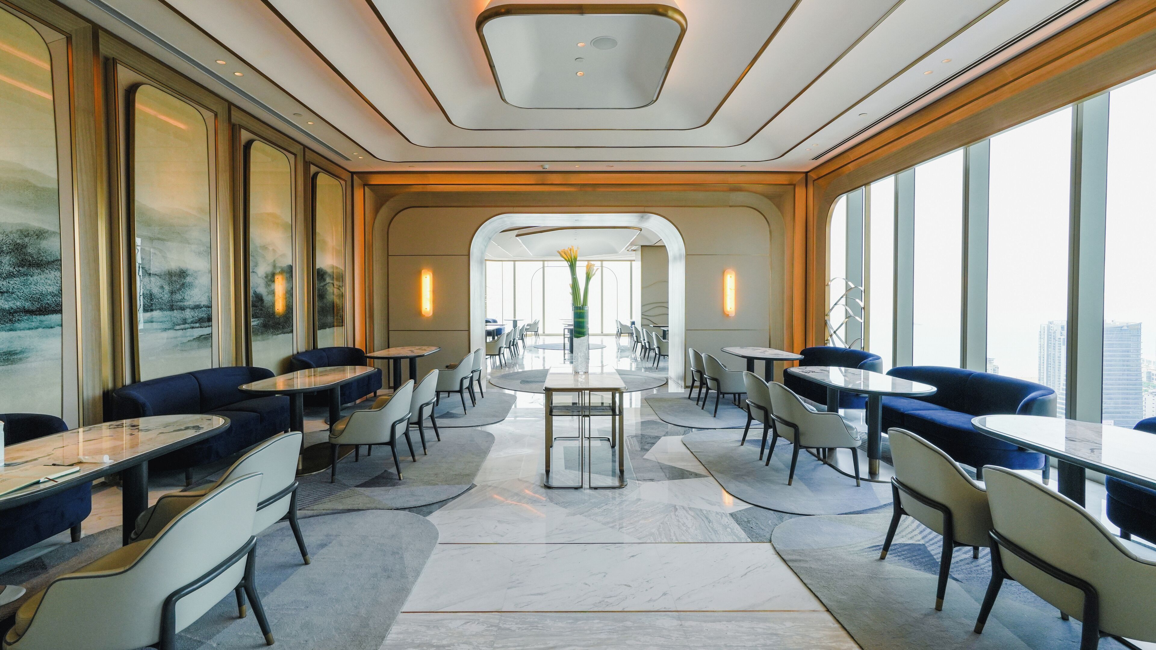 A modern dining area with round tables and chairs, large windows, and a view of the city.