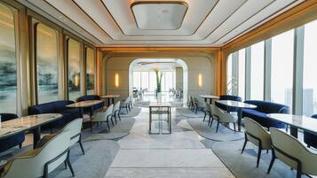 A modern dining area with round tables and chairs, large windows, and a view of the city.
