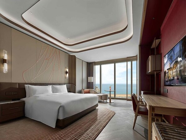A modern hotel room with a large bed, a desk, and a view of the ocean. - MGM Qingdao (Qingdao)
