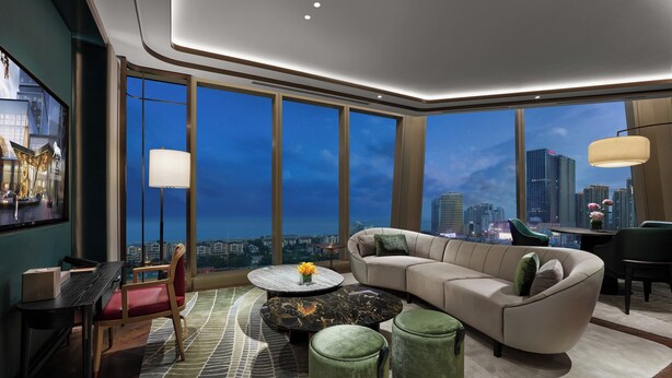 A modern living room with a large window, a sofa, a coffee table, and a view of a cityscape. - MGM Qingdao (Qingdao)