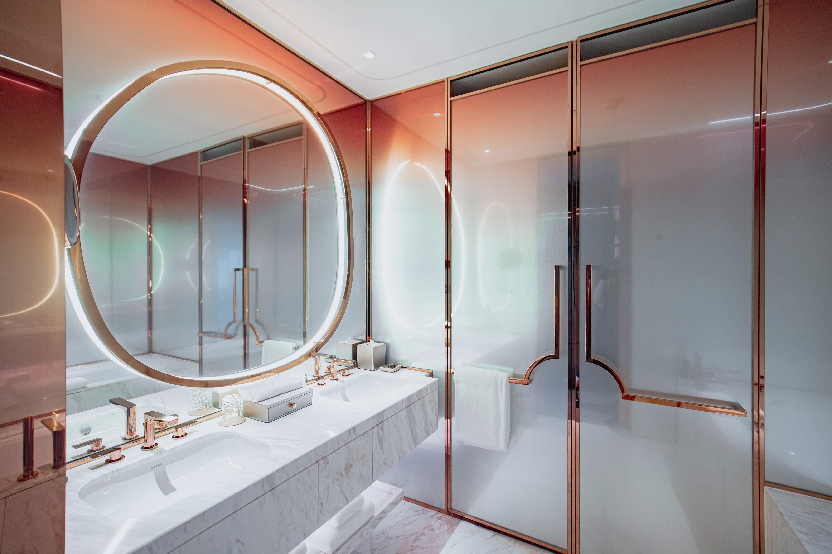 A modern bathroom with a large mirror, two sinks, and a glass shower enclosure.