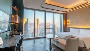 A modern hotel room with a large window, a round table, a sofa, and a bed. - MGM Qingdao (Qingdao)