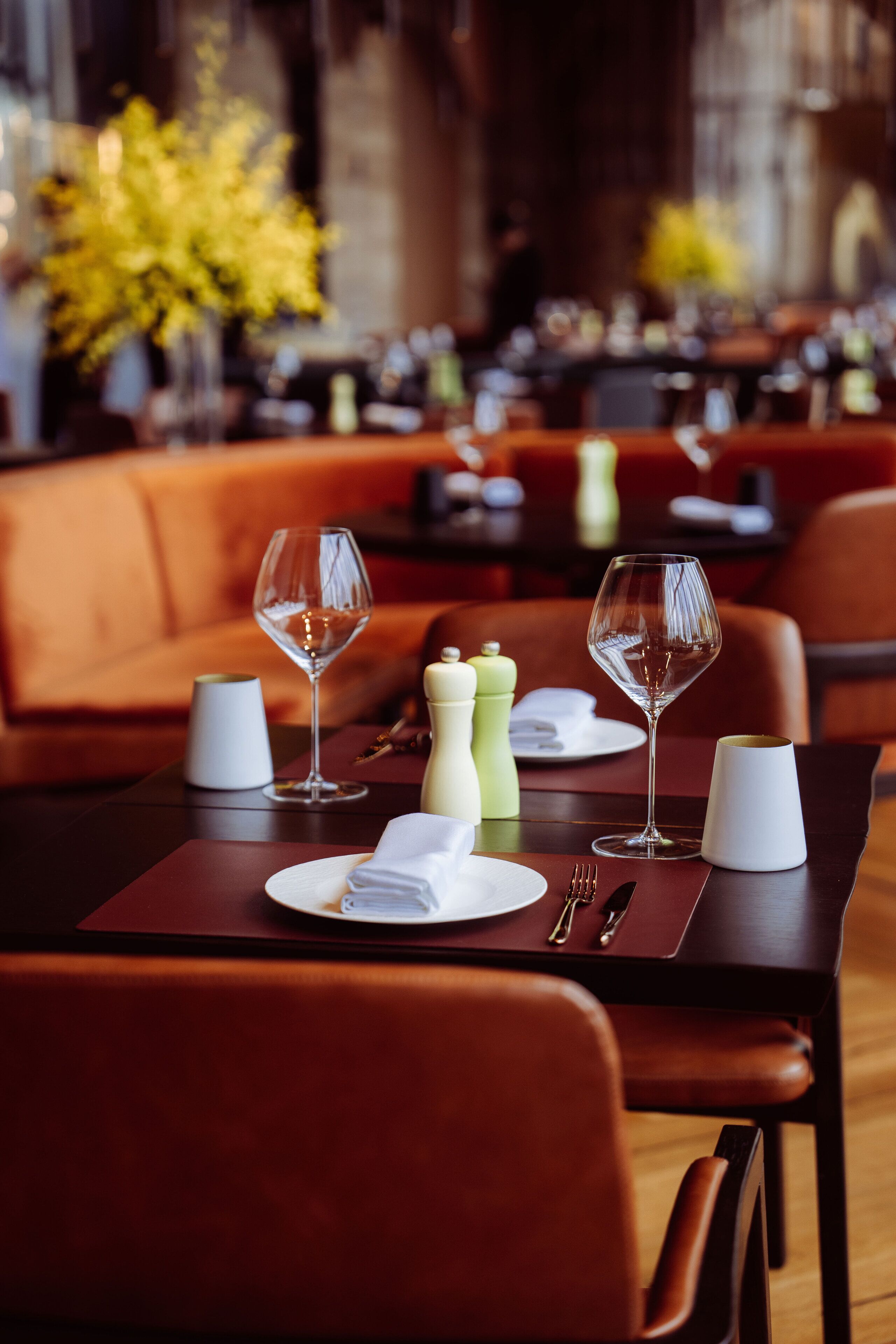 A restaurant setting with a table set for two, featuring wine glasses, plates, cutlery, and a salt and pepper shaker.