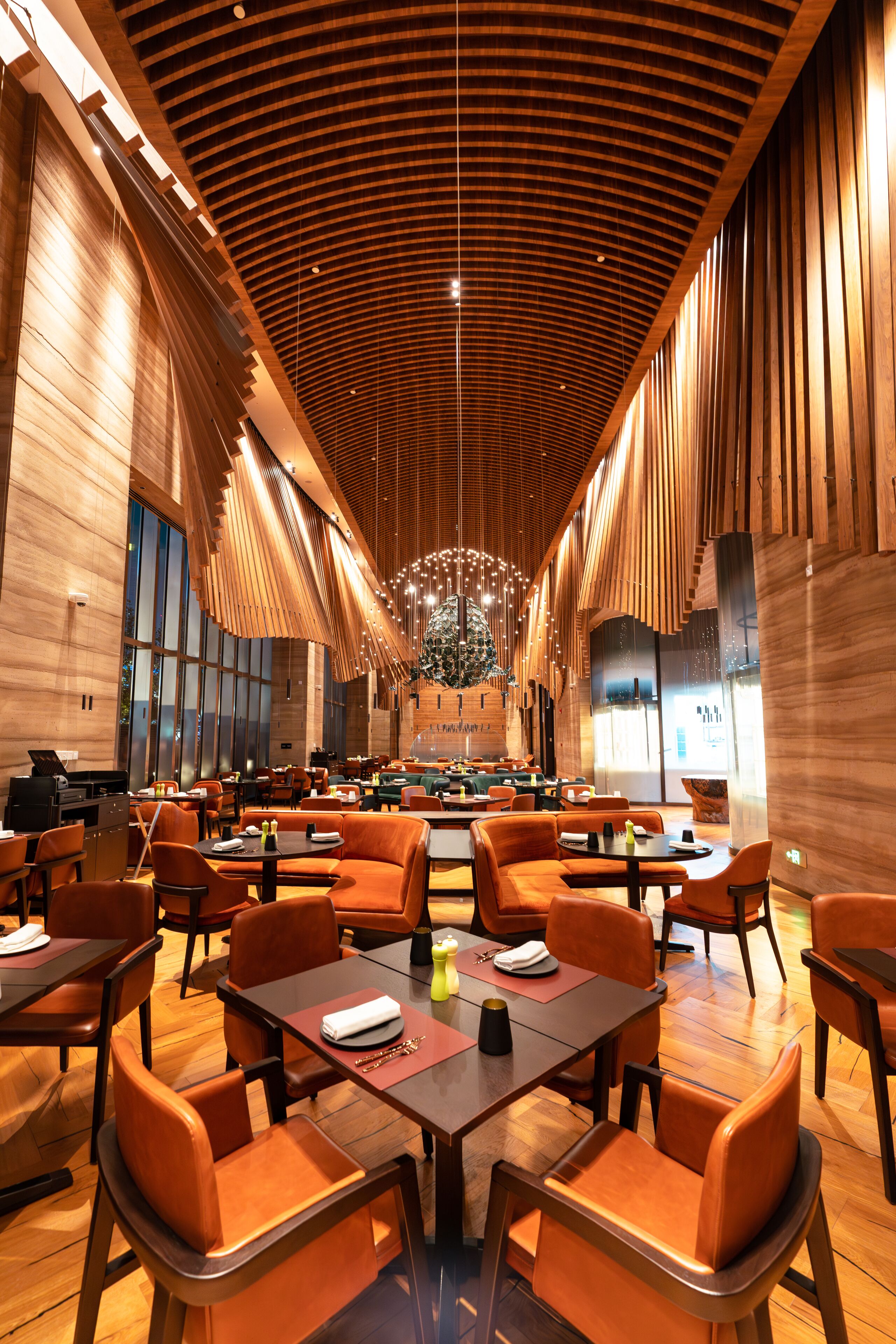A spacious restaurant with high ceilings, wooden paneling, and modern orange seating.
