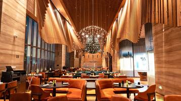 A spacious restaurant with high ceilings, wooden paneling, and modern orange seating.