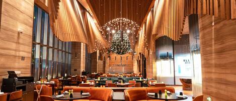 A spacious restaurant with high ceilings, wooden paneling, and modern orange seating.