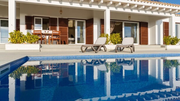 A poolside area with lounge chairs, a dining table, and a covered patio. - Bini Sole - Luxury villa with pool in Menorca (Sant Lluís)