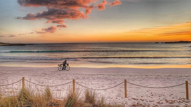 A beach with a person on a bicycle, a wooden fence, and a sunset over the ocean. - Casa Lola - Serene and luxurious apartment with balcony (Ciutadella de Menorca)