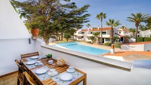 A poolside dining area with a table set for four, overlooking a swimming pool and a residential complex. - Casa Lola - Serene and luxurious apartment with balcony (Ciutadella de Menorca)