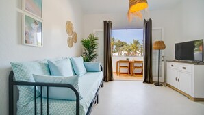 A modern living room with a sofa, a TV, a dining table, and a view of palm trees through the window. - Casa Lola - Serene and luxurious apartment with balcony (Ciutadella de Menorca)