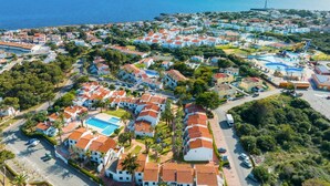 An aerial view of a coastal residential area with houses, a swimming pool, and a lighthouse in the background. - Casa Lola - Serene and luxurious apartment with balcony (Ciutadella de Menorca)
