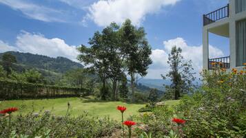 Un jardin luxuriant, avec une grande variété de fleurs et d’arbres, une pelouse bien entretenue et une vue sur des collines lointaines.